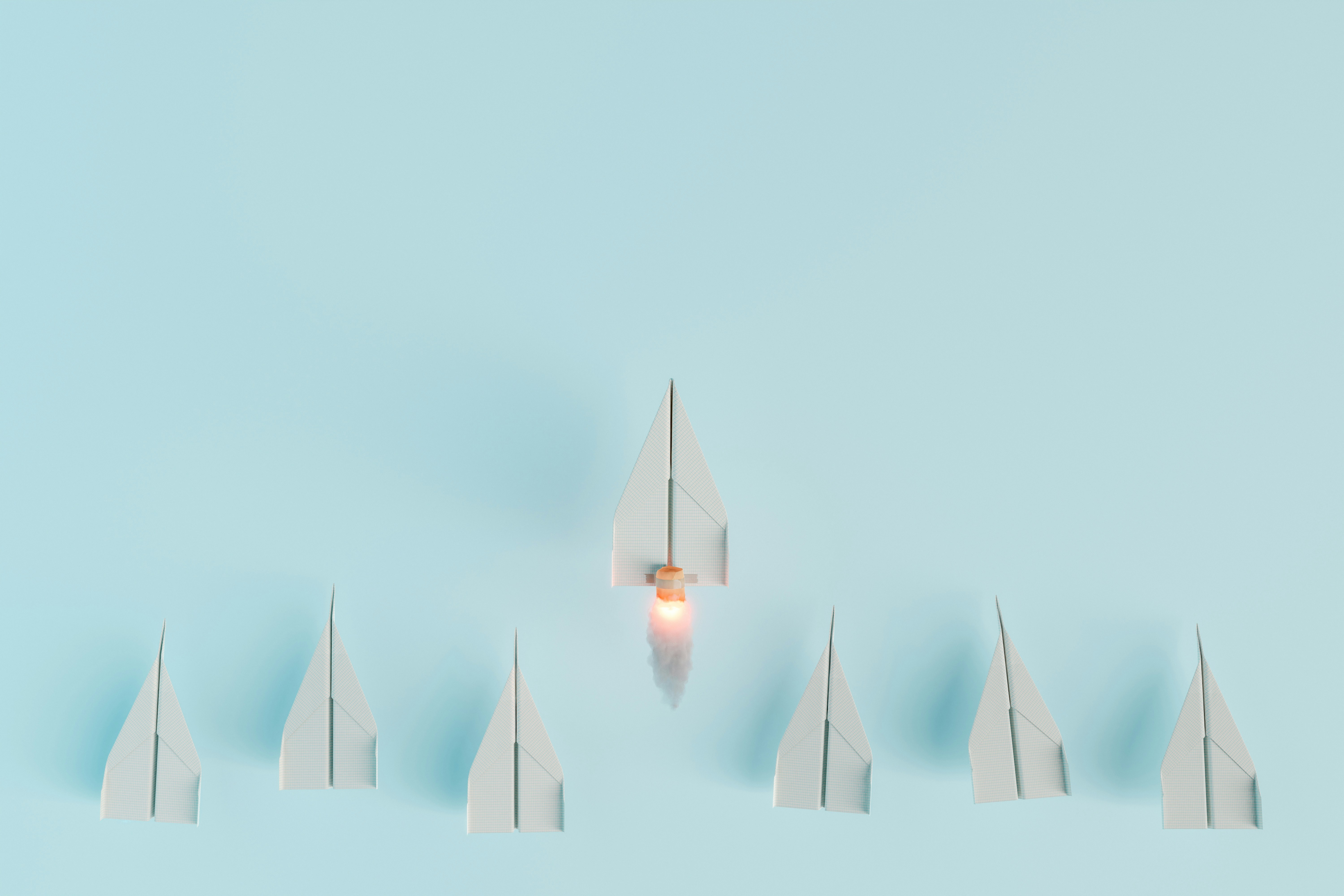 Conceptual image of paper airplanes arranged in a V-formation with one central airplane launching upward using a rocket booster, symbolizing innovation, leadership, and standing out from the crowd.